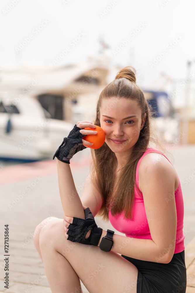 Young pretty sport girl at outdoors holding an orange