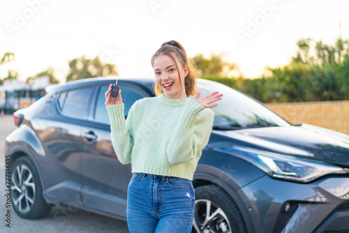 Young pretty girl holding car keys at outdoors points finger at you with a confident expression