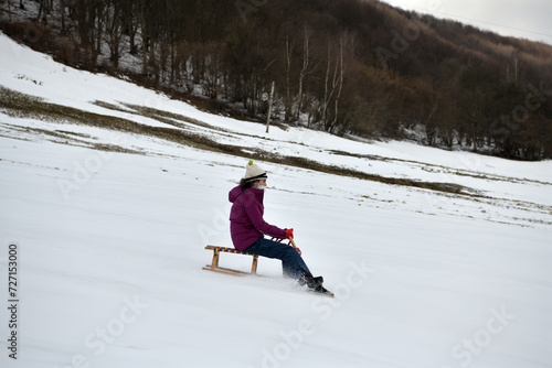 Girl sledding downhill on snow in winter and laughing with joy