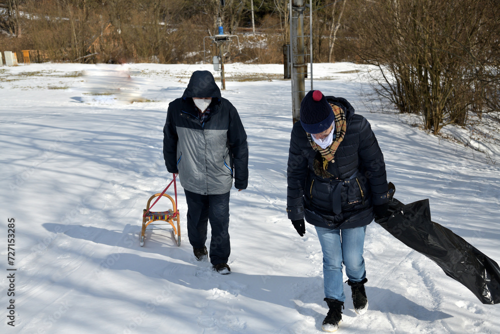 Men and women are pulling sledge up the hill in the winter in the snow