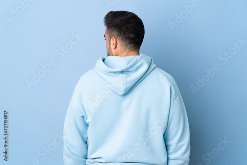 Caucasian man over isolated blue background in back position and looking side © luismolinero