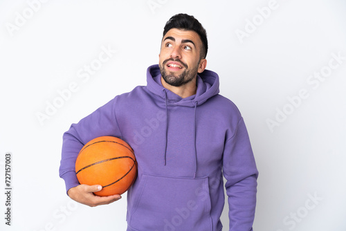 Man playing basketball over isolated white wall thinking an idea while looking up