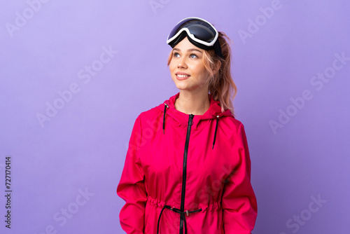 Skier teenager girl with snowboarding glasses over isolated purple background thinking an idea while looking up © luismolinero