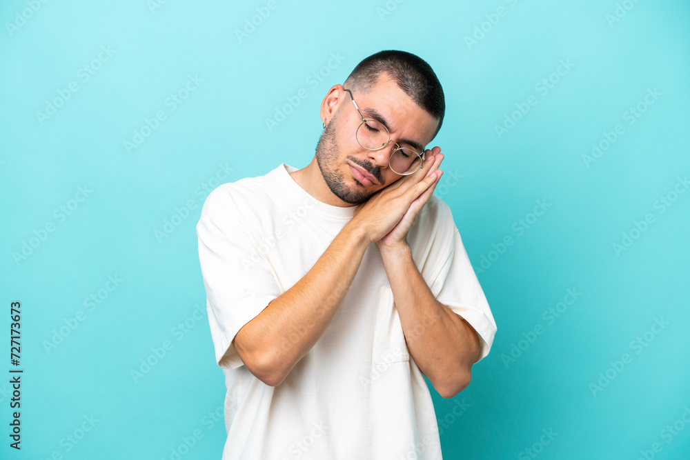 Young caucasian man isolated on blue background making sleep gesture in dorable expression Young caucasian man isolated on blue background making sleep gesture in dorable expression