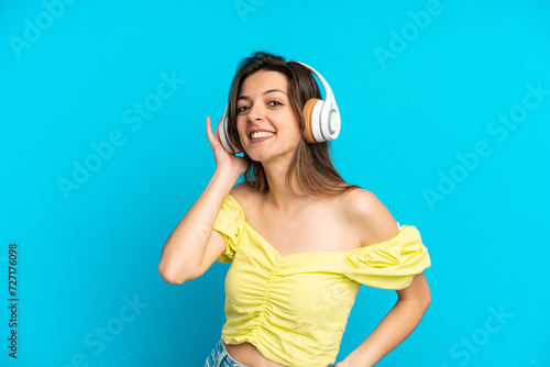 Young caucasian woman isolated on blue background listening music