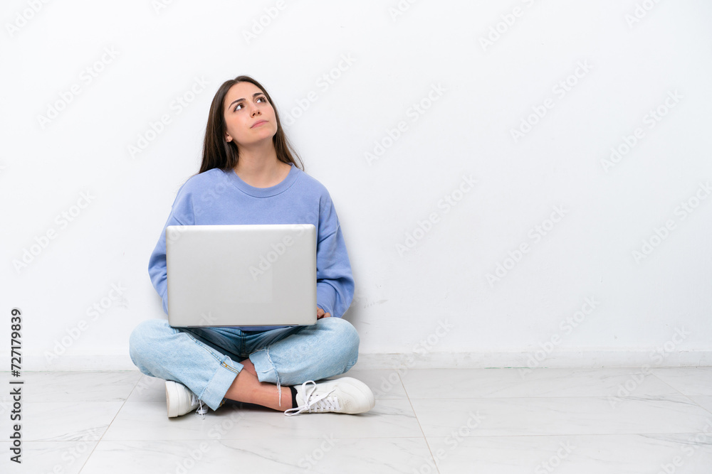 Young caucasian woman with laptop sitting on the floor isolated on white background and looking up Young caucasian woman with laptop sitting on the floor isolated on white background and looking up