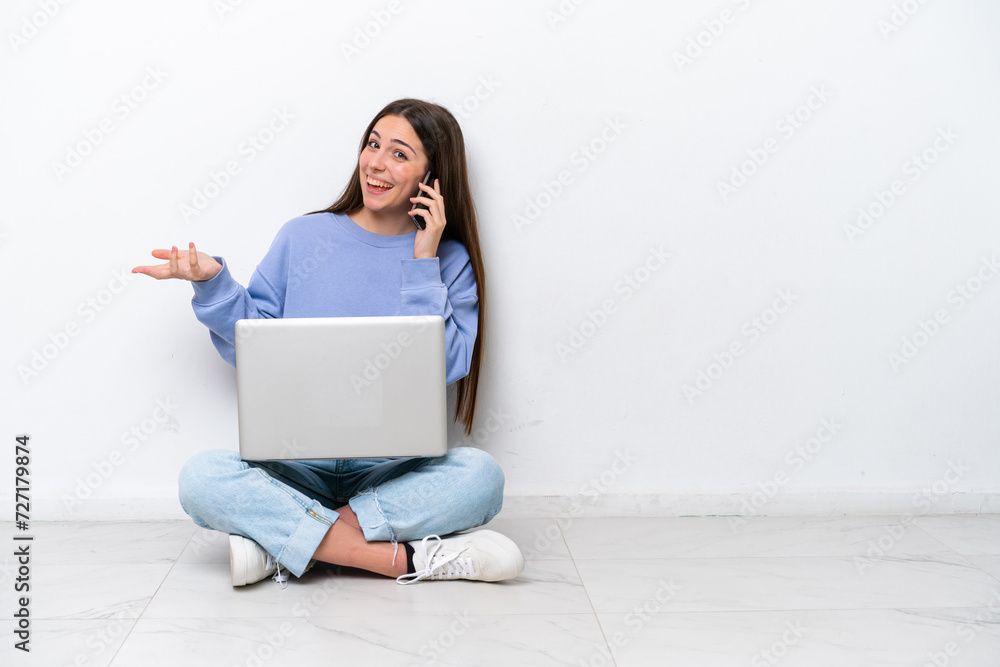 Young caucasian woman with laptop sitting on the floor isolated on white background keeping a conversation with the mobile phone with someone Young caucasian woman with laptop sitting on the floor isolated on white background keeping a conversation with the mobile phone with someone