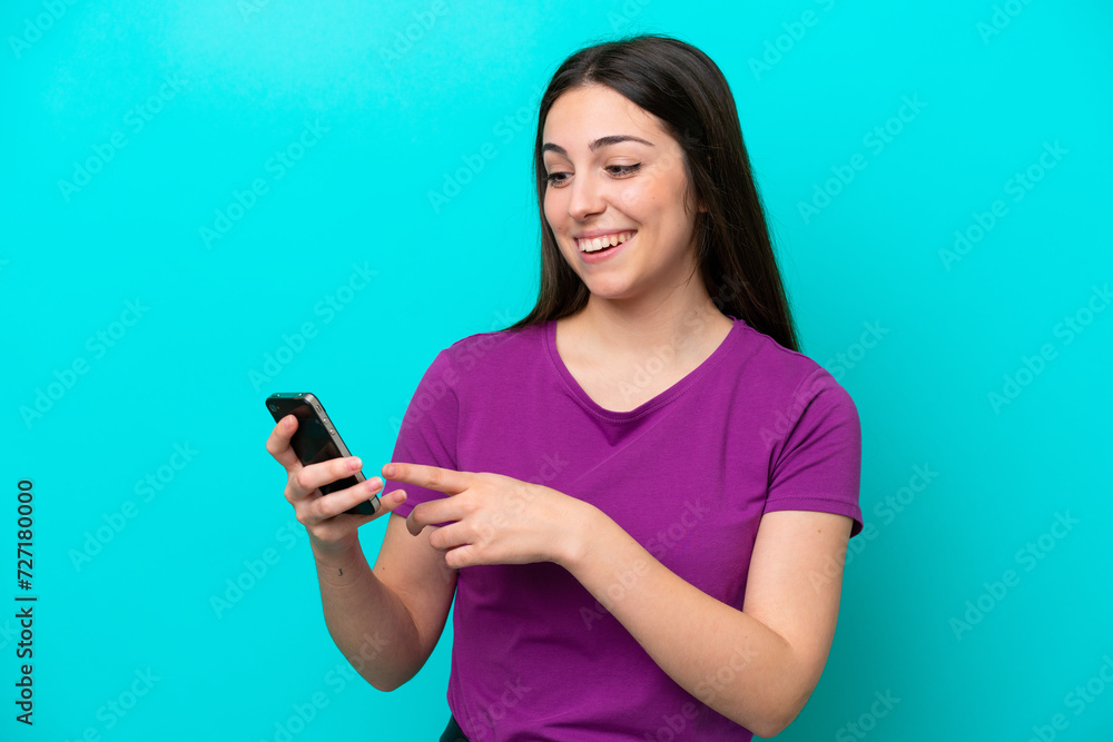 Young girl isolated on blue background sending a message or email with the mobile Young girl isolated on blue background sending a message or email with the mobile