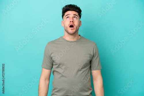 Young caucasian man isolated on blue background looking up and with surprised expression