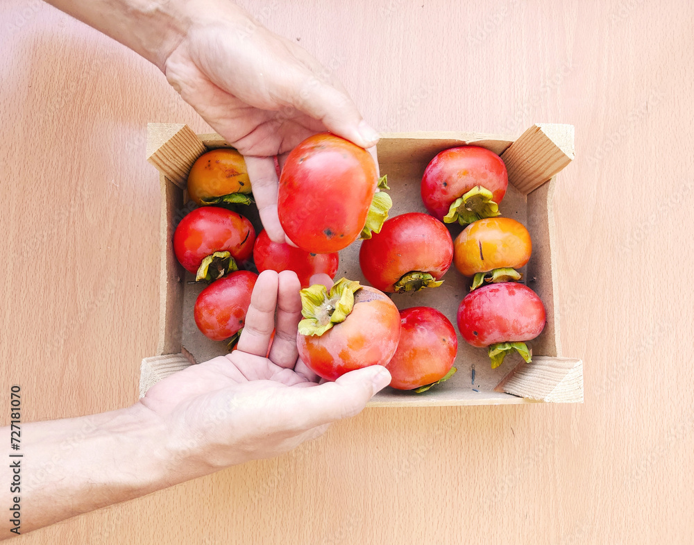 Close up man hands hold a wooden box with organic persimmons. Close up man hands hold a wooden box with organic persimmons.