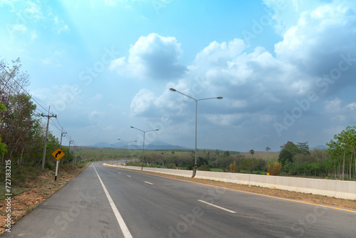 Curved asphalt road with gurad lense and trees on beside. Under blue sky in the countryside of Thailand. Light shining through the shadows of the trees. photo