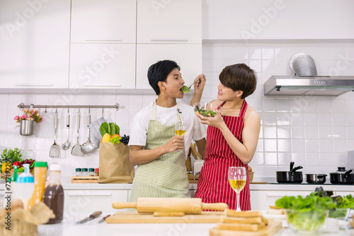 Cute Asian gay man feed salad to his lgbtq partner in kitchen