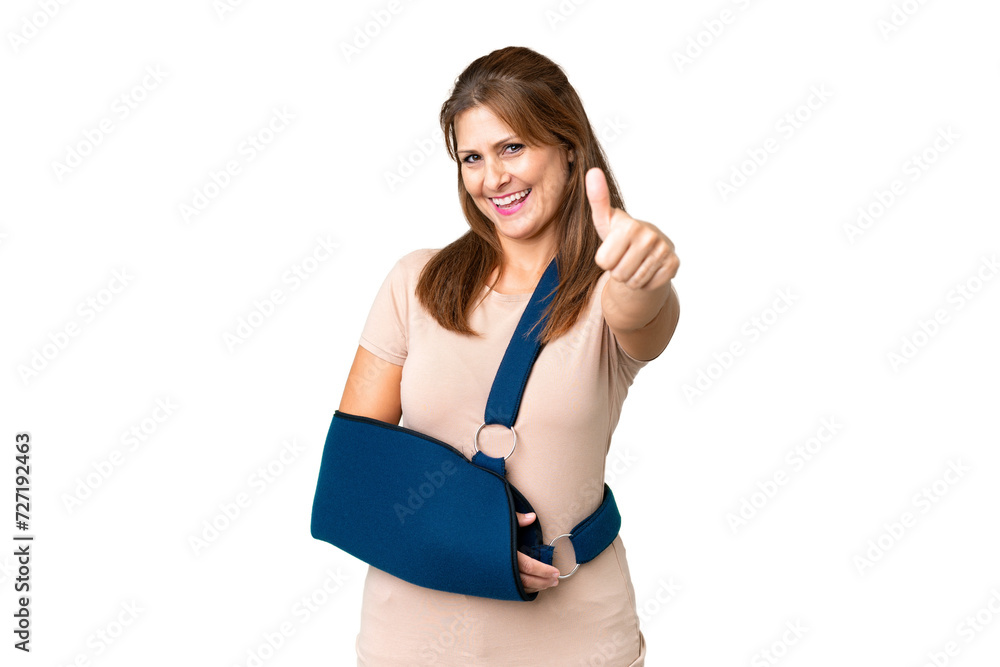 Middle age with broken arm and wearing a sling over isolated background with thumbs up because something good has happened Middle age with broken arm and wearing a sling over isolated background with thumbs up because something good has happened