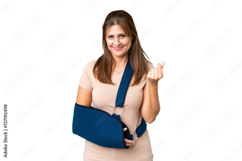 Middle age with broken arm and wearing a sling over isolated background making money gesture Middle age with broken arm and wearing a sling over isolated background making money gesture