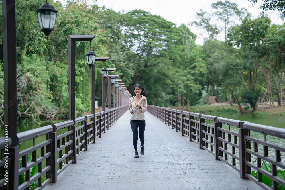 Young asian sporty women wearing earphones to listening the music on smartphone and running in the park while workout and fitness exercise for healthy wellness lifestyle in morning at outdoor jogging