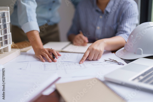 Two architects discuss about building project on blueprint with construction plan and taking notes