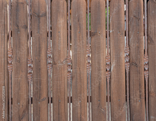 Fragment of a fence made of wooden boards and brown iron rods.