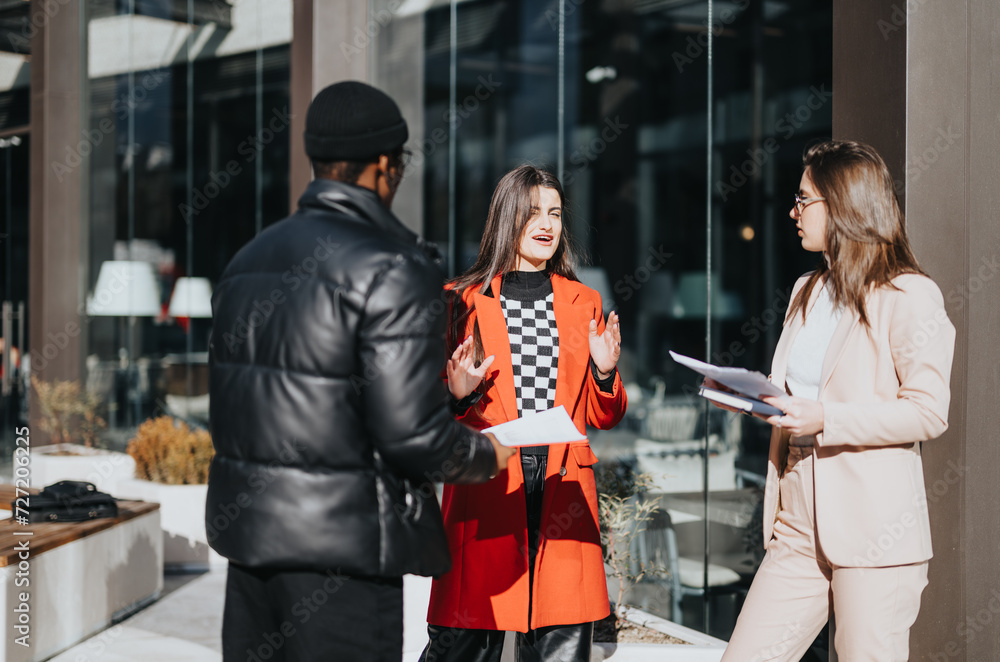 Obraz premium Two women and a man in professional attire engage in a casual business conversation outside a modern office building on a sunny day.