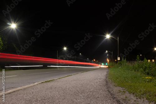 Nighttime cityscape - bright streetlights - red and white light trails streak across the road - passing vehicles long exposure. Taken in Toronto, Canada. © Jacob Tian