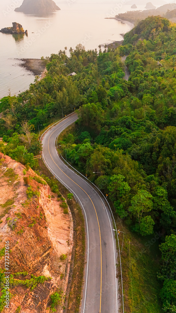 Aerial view with road passing through green forest and mountains. Top-angle photograph of the road outside the city and the large forest. Top view for use as background. Nature, vacation, travel.
