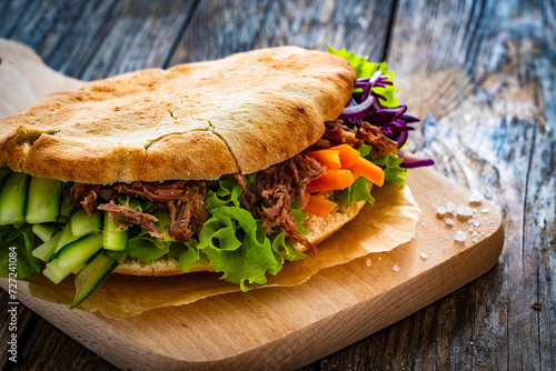 Pita - big sandwich with pulled beef and fresh vegetables on wooden table
 photo