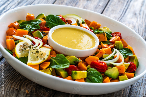 Tasty salad - baked sweet potatoes, avocado, spinach and tomatoes with tahini sauce on wooden table
 photo