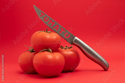 Knife with the inscription Tomato  lies on the tomato vegetable isolated over red background. © Naz