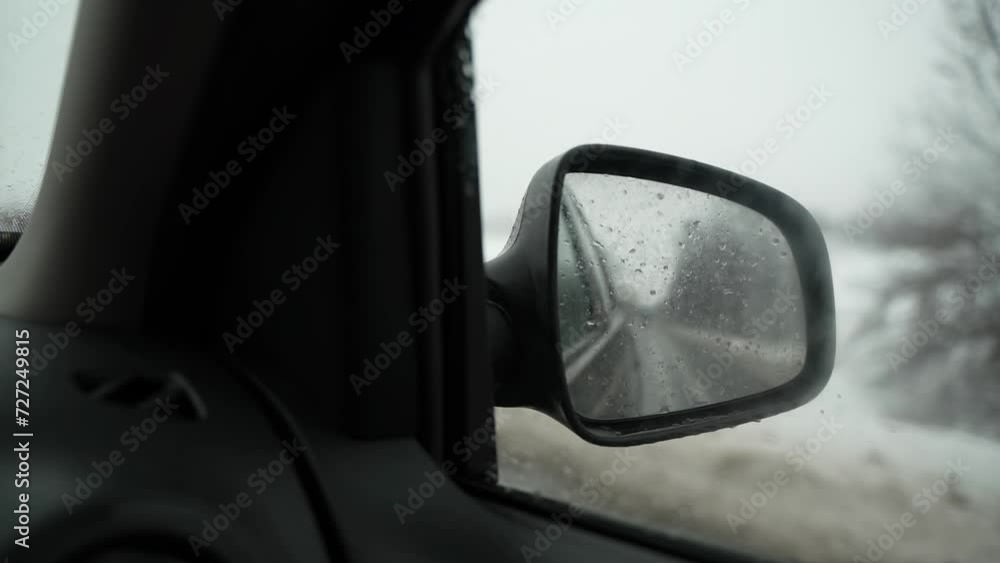 POV from inside the car on the side rear view mirror while driving on a wet snowy road. Raindrops on the side window and mirror of the car. Traveling on a winter or spring day. POV from inside the car on the side rear view mirror while driving on a wet snowy road. Raindrops on the side window and mirror of the car. Traveling on a winter or spring day.