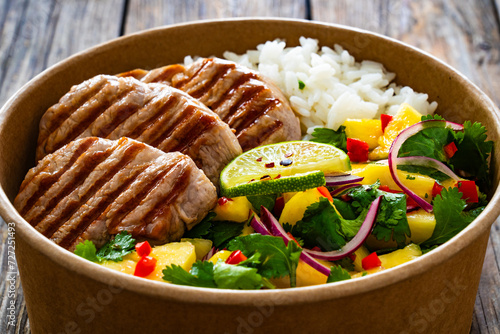Grilled pork loin steaks with rice and mango salad in lunch box to go on wooden table
 photo