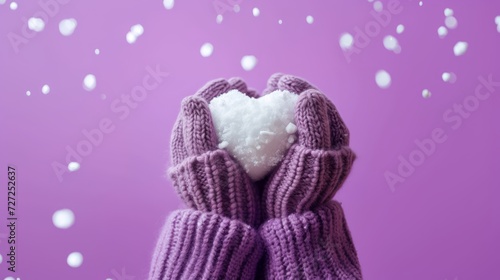 Hands in lilac knitted woolen mittens hold heart shaped snowball, banner, lilac background