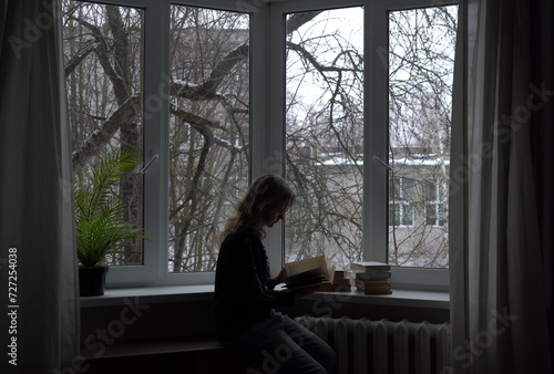 A woman with books sits near the window.