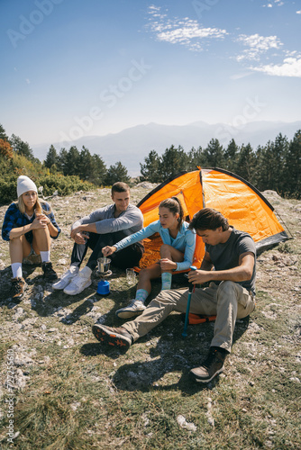 Four hikers relaxing while sitting and making coffee at the mountain