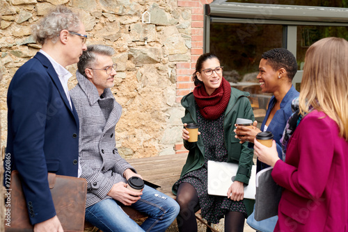 Informal meeting of colleages outdoors. Business meeting with coffee in an outdoor cafe. Five business partners with takeaway coffee talking in the street in informal style. photo