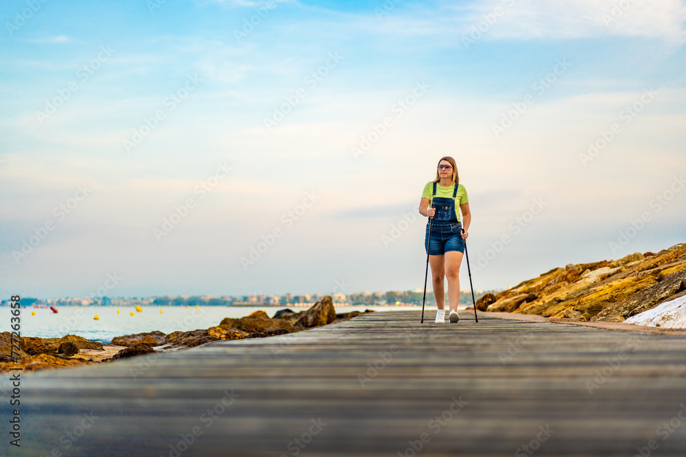 Mid adult woman exercising Nordic walking on seaside boulevard - Costa Dorada Spain
