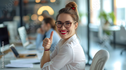woman with glasses is smiling and giving a thumbs up in an office environment