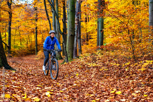 Woman riding bicycle in city forest in autumn scenery