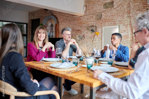 Multiethnic team having business lunch in restaurant sitting at served table with red wine in glasses and having conversation. photo