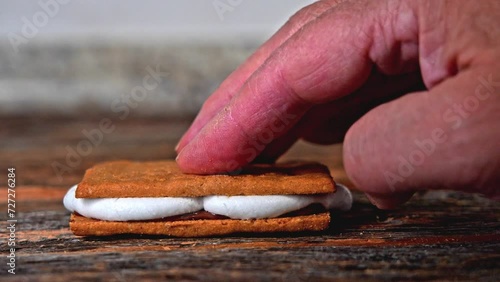 Hand making snack sandwich with graham crackers,marshmallow and chocolate on rustic wood photo