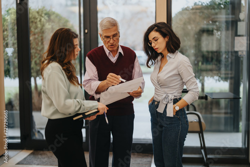 Fényképezés A seasoned business leader reviews paperwork with two professional women in an office environment, conveying teamwork and collaboration