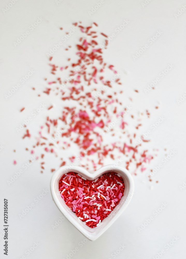 Heart shaped bowl full of pink confetti on white background