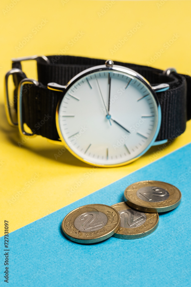 A hand watch with a white shield and tips lying on a yellow-blue background. Next to the Polish coins of PLN. Photo concept A hand watch with a white shield and tips lying on a yellow-blue background. Next to the Polish coins of PLN. Photo concept