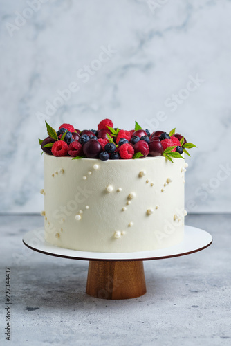 Delicious and beautiful handmade cake. Confectionery for the holiday. The dessert is decorated with fresh raspberries, cherries and blueberries.