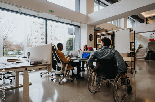 Modern office setting showcasing diversity with a man in a wheelchair and multiethnic colleagues working.