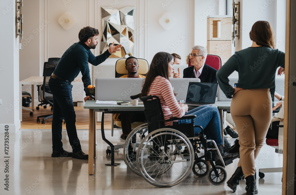 A cross generational group of professionals engage in a business meeting. The image includes a person using a wheelchair, depicting inclusivity and teamwork in a modern office setting. A cross generational group of professionals engage in a business meeting. The image includes a person using a wheelchair, depicting inclusivity and teamwork in a modern office setting.