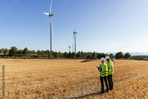 Obraz na plátně Team of engineers standing in the field inspecting the operation of wind turbines