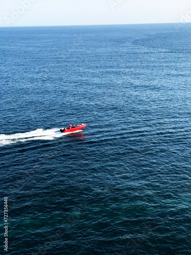 Red boat on the sea background: a boat with red colouring on the smooth water of the sea. The photo conveys the dynamics and beauty of a sea voyage on a red boat