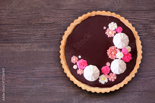 Delicious chocolate tart with meringue and pink chocolate flowers. Above view on a dark wood background. Spring baking concept.
