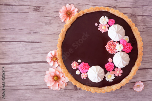 Sweet chocolate tart with meringue and pink chocolate flowers. Top view table scene with flowers on a wood background. Spring baking concept.