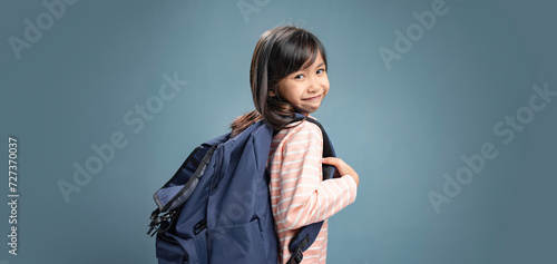 A little girl is carrying a school bag and smiling.