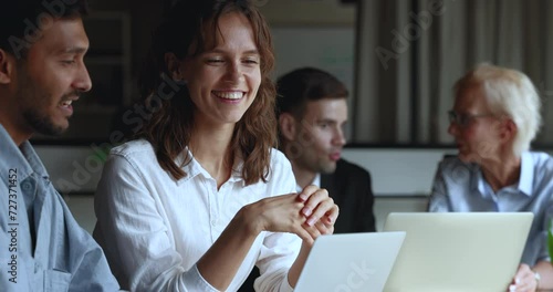 Young multiethnic business colleagues talking at laptop, sitting at meeting table, looking and pointing at screen. Positive Indian mentor man training listening, nodding intern woman at computer